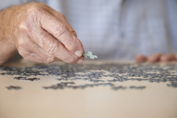 Elderly man, aged 77, looking for pieces of a jigsaw puzzle in a private retirement home